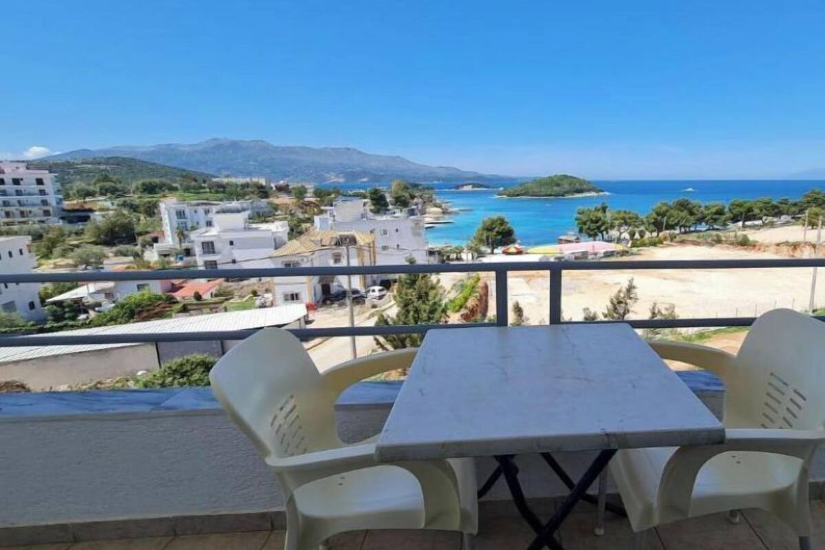 A balcony with a table and chairs overlooking a coastal view with buildings and a beach.