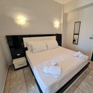 A neatly made bed with white linens and towels, a black headboard, and a nightstand with a drawer. - Hotel Ardiani (Sarandë)