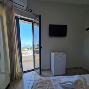Hotelkamer met een bed, een kleine witte koelkast, een aan de muur bevestigde televisie en een schuifdeur naar een buitenbalkon.