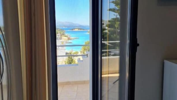 Une pièce dotée d’une porte-fenêtre coulissante donnant sur un balcon avec vue sur la mer et le paysage lointain.