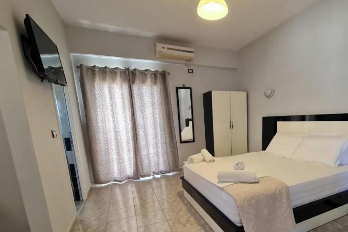 Une chambre d’hôtel équipée d’un lit, d’une armoire, d’un téléviseur à écran plat fixé au mur et d’une fenêtre avec des rideaux.