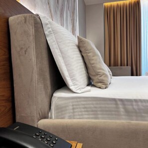 A hotel room with a bed, pillows, and a remote control on a wooden surface. - Hotel Memmaj (Ksamil)