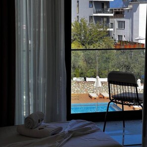 A hotel room with a bed, a window with curtains, and a view of a pool and buildings. - Hotel Memmaj (Ksamil)