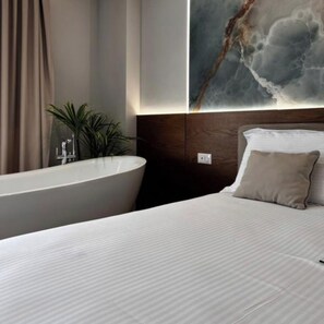 A modern hotel room with a large bed, a freestanding bathtub, and a wall-mounted artwork. - Hotel Memmaj (Ksamil)