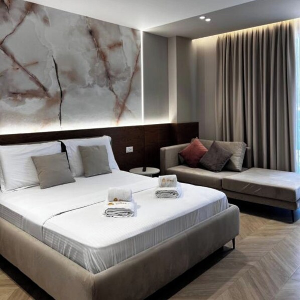 A modern hotel room with a large bed, a sofa, and a marble wall. - Hotel Memmaj (Ksamil)