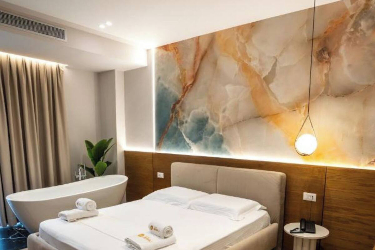 A modern hotel room with a large bed, a bathtub, and a marble wall.