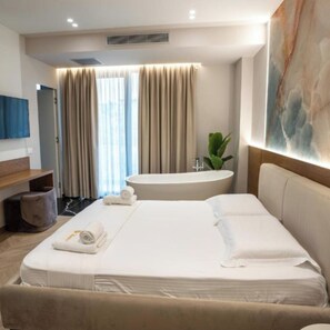 A modern hotel room with a large bed, a built-in bathtub, and a large window with curtains. - Hotel Memmaj (Ksamil)