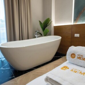 Une salle de bain avec une baignoire sur pieds, une serviette ornée d’un logo et une plante en pot.