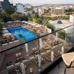 A rooftop pool area with lounge chairs and umbrellas, surrounded by stone walls and greenery, overlooking a cityscape. - Hotel Memmaj (Ksamil)