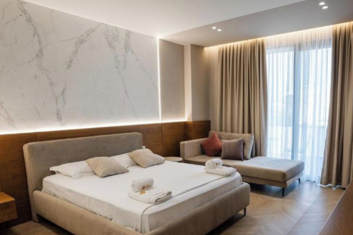 A modern hotel room with a large bed, a sofa, and a desk.