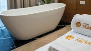 Une salle de bain avec une baignoire sur pieds, une serviette ornée d’un logo et une plante en pot.