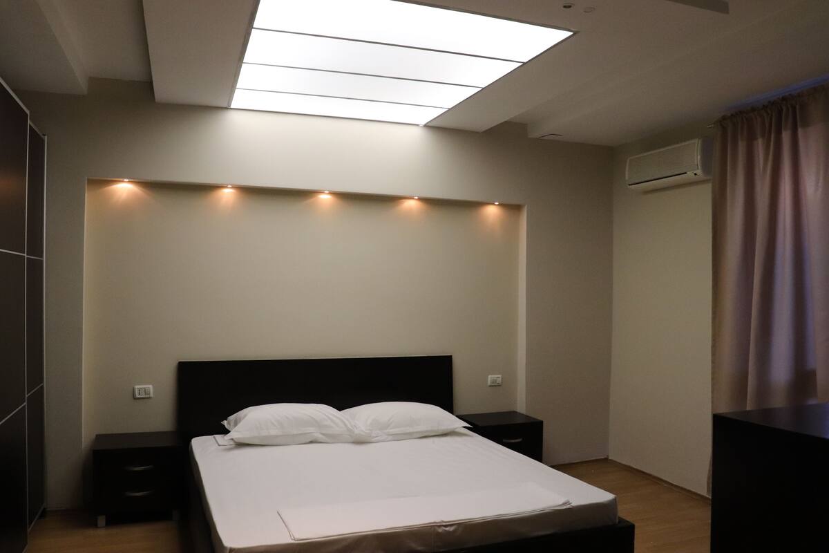 A modern bedroom with a skylight, a bed with white linens, a nightstand, and a dresser.