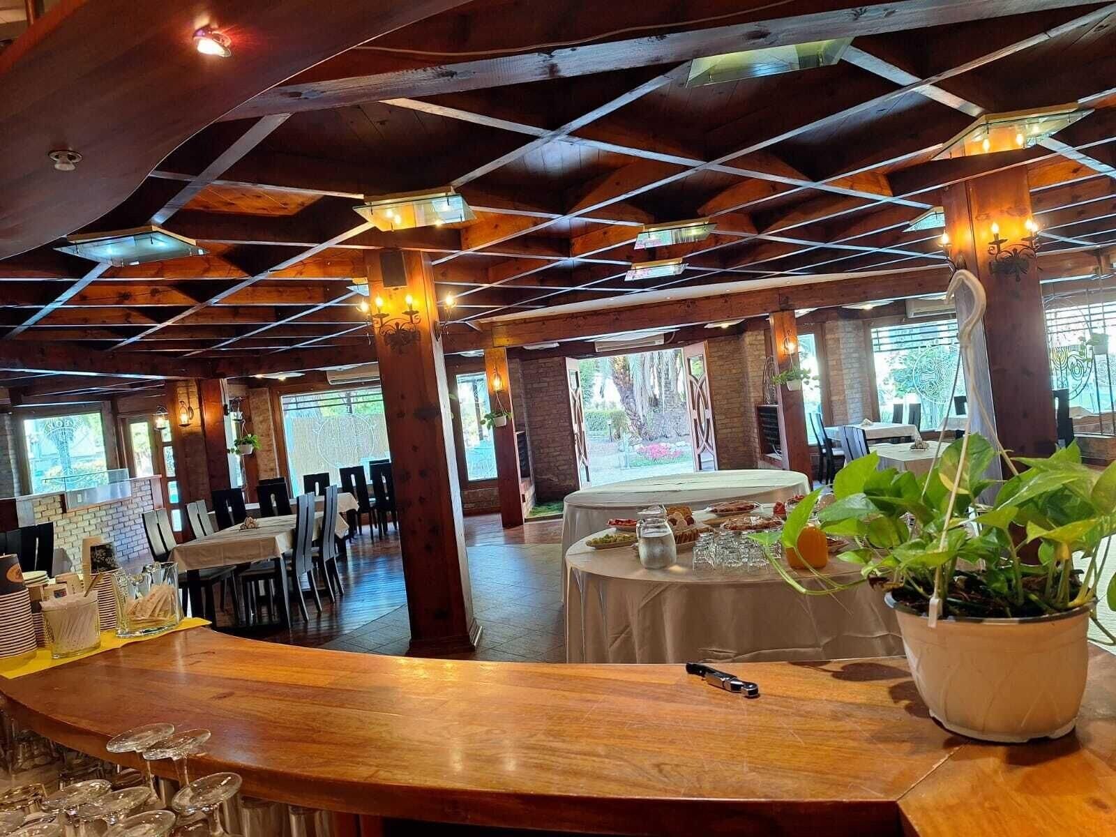 A restaurant with wooden beams, tables, chairs, and potted plants.