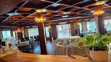 A restaurant with wooden beams, tables, chairs, and potted plants.