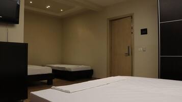Habitación de hotel con dos camas individuales, una puerta de madera y un televisor montado en la pared.