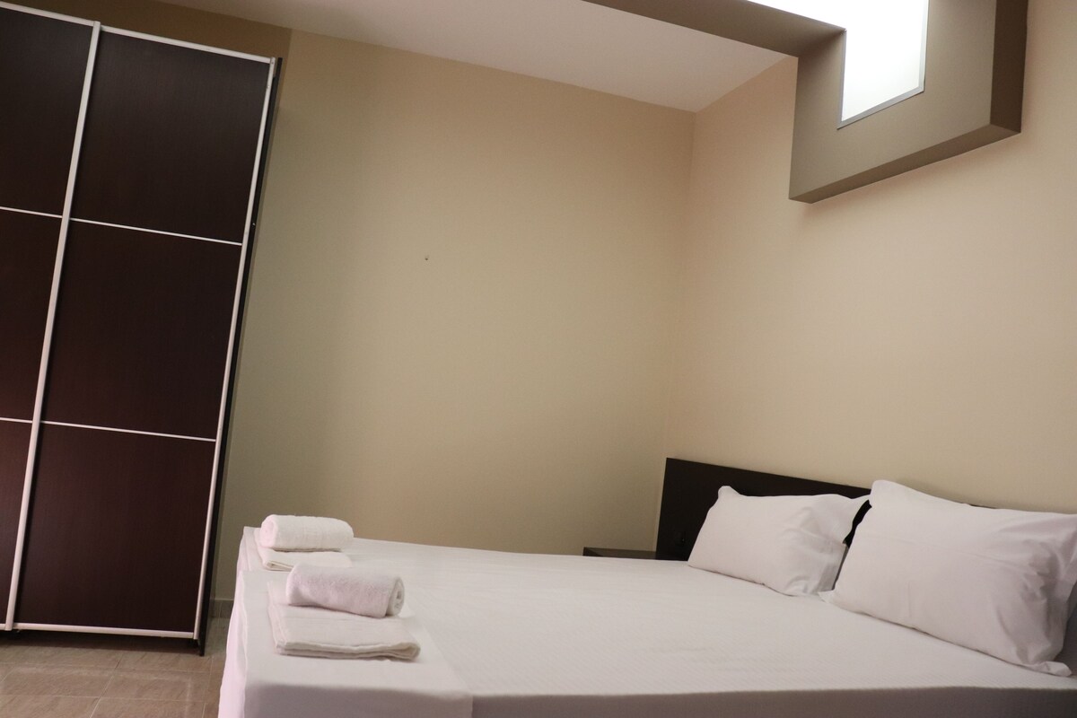 A hotel room with a bed, white linens, a dark headboard, a large window, and a sliding door.