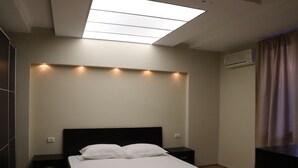 A modern hotel room with a skylight, a bed with white linens, a nightstand, and an air conditioning unit. - Danis Hotel (Tirana)