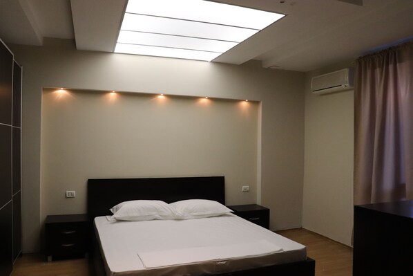 A modern hotel room with a skylight, a bed with white linens, a nightstand, and an air conditioning unit. - Danis Hotel (Tirana)