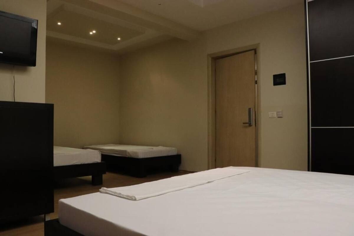 A hotel room with a large bed, two smaller beds, a TV, and a door.