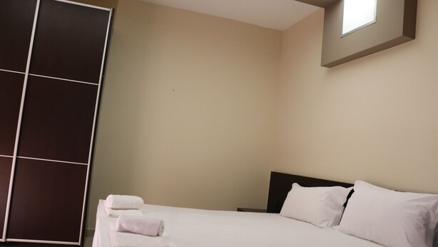 A hotel room with a bed, white linens, a dark headboard, a large window, and a sliding door.