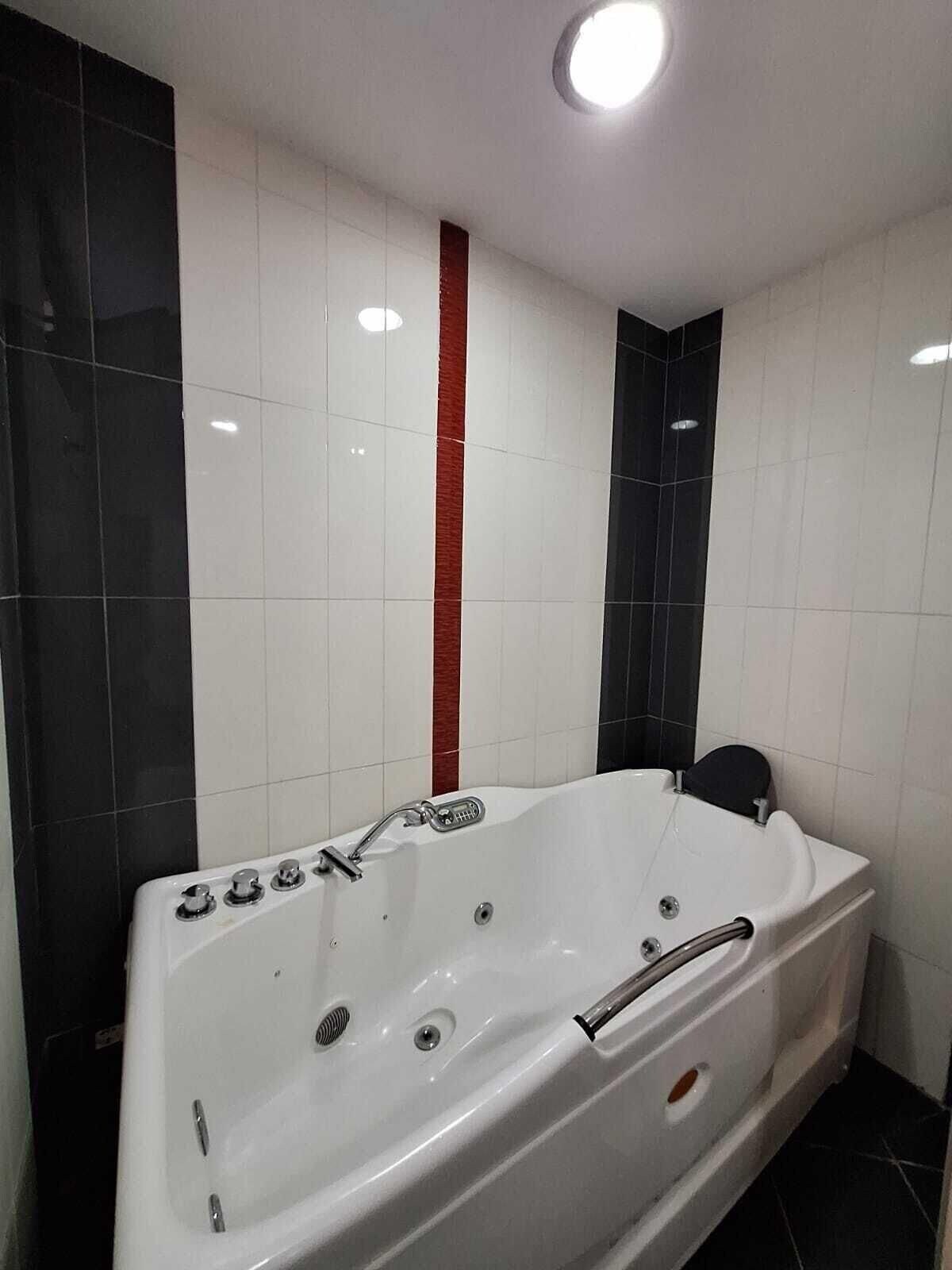 A modern bathroom with a white bathtub, black and white tiled walls, and a red accent strip.