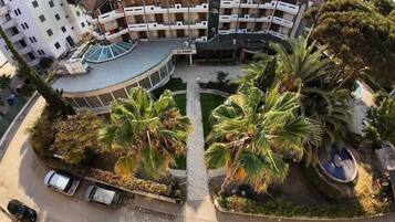A multi-story hotel with a central courtyard, palm trees, and a swimming pool.
