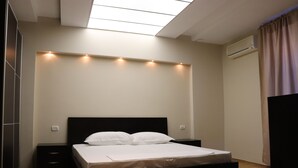 A bedroom with a bed, bedside tables, a ceiling light fixture, and an air conditioning unit. - Danis Hotel (Tirana)