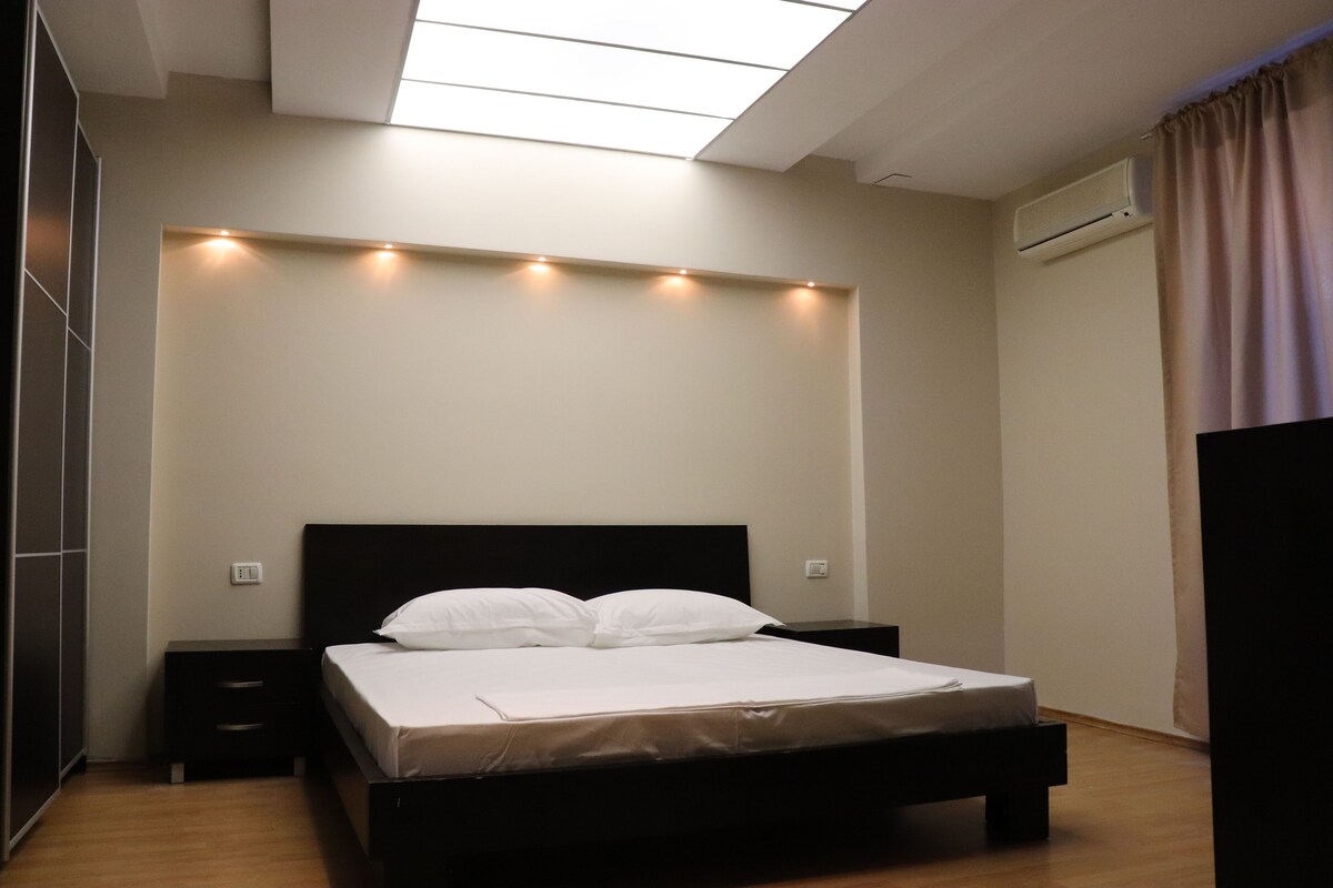 A bedroom with a bed, bedside tables, a ceiling light fixture, and an air conditioning unit.