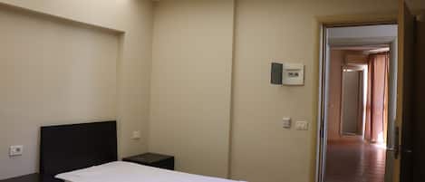 A bedroom with a bed, bedside tables, a ceiling light, and a door leading to another room.