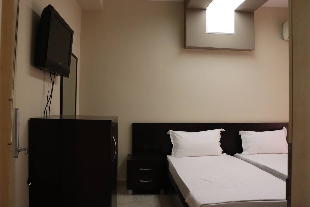 A hotel room with a bed, a TV mounted on the wall, and a small window.