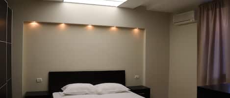 A modern hotel room with a skylight, a bed with white linens, a nightstand, and an air conditioning unit.