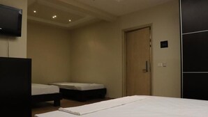 A hotel room with a large bed, two smaller beds, a TV, and a door. - Danis Hotel (Tirana)