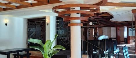 A spacious indoor area with wooden beams, a central column, and a seating arrangement.