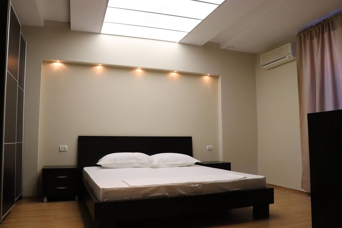 A bedroom with a bed, bedside tables, a wardrobe, and a skylight.