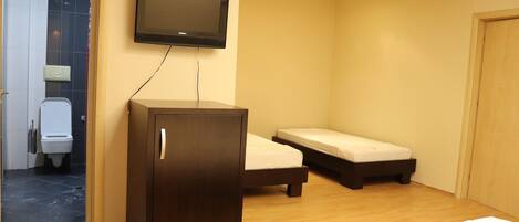 A room with a television mounted on the wall, a wooden cabinet, a bed, and a small bedside table.