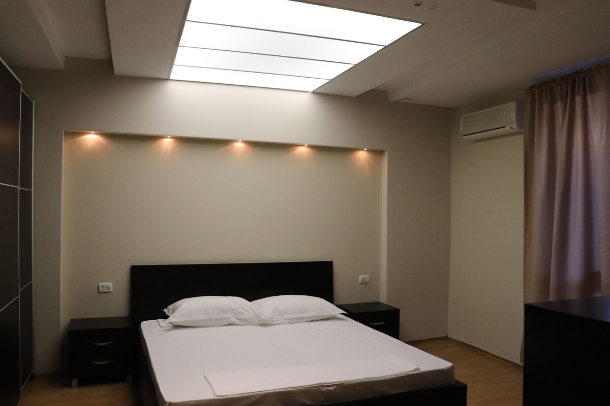 A modern bedroom with a skylight, a bed with white linens, a nightstand, and a dresser.