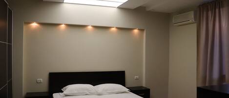 A modern bedroom with a skylight, a bed with white linens, a nightstand, and a dresser.