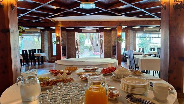 A breakfast buffet with various food items and beverages, set in a room with wooden beams and large windows. - Danis Hotel (Tirana)