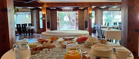 Un bufé de desayuno con diversas opciones de comida y bebidas, en un espacio con vigas de madera y ventanas amplias.
