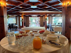 Ein reichhaltiges Frühstücksbuffet mit verschiedenen Speisen und Getränken, in einem Raum mit Holzbalken und großen Fenstern.