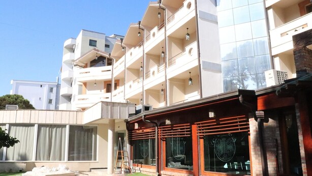 A multi-story building with balconies, a covered outdoor seating area, and a paved courtyard. - Danis Hotel (Tirana)