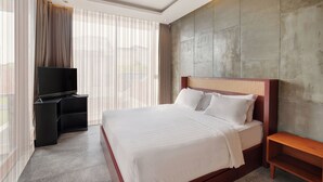 A hotel room with a large bed, a TV on a stand, and a window with curtains. - Aqilah Villa Bali (Legian)