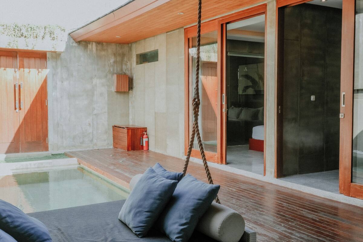 Een modern buitengebied met een zwembad, een houten terras en een schuifdeur naar een slaapkamer.