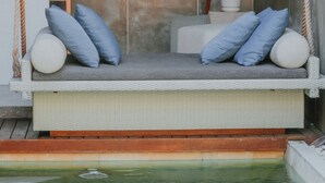 A cozy outdoor seating area with a swing, cushions, a lamp, and a view of the water. - Aqilah Villa Bali (Legian)