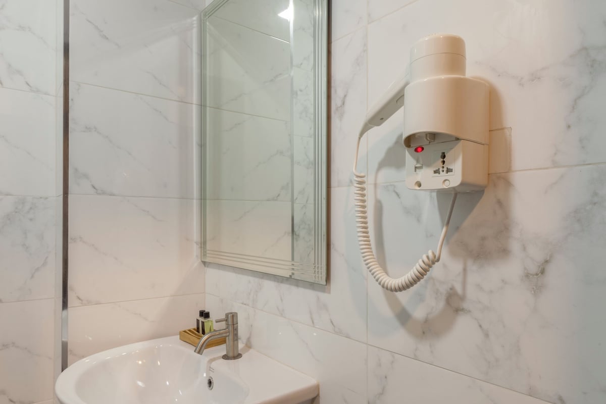 A bathroom with a white marble sink, a mirror, and a hairdryer mounted on the wall.