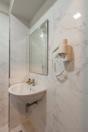 A bathroom with a white marble sink, a mirror, and a hairdryer mounted on the wall. - Rcn Court (Chiang Mai)