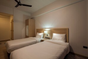 Een hotelkamer met twee eenpersoonsbedden, een nachtkastje met een lamp, een plafondventilator en een kledingkast.