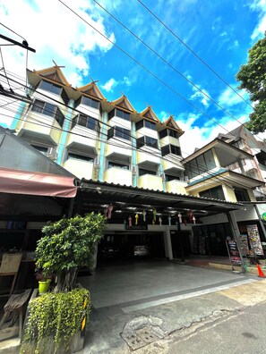 Un edificio de varios pisos con un estilo arquitectónico tradicional, con balcones y un área de entrada cubierta decorada con adornos colgantes.