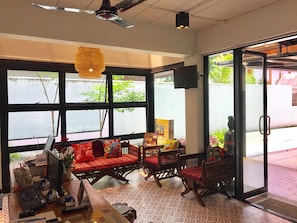 A room with large windows, a ceiling fan, a TV, and a desk with a computer and various items. - Rcn Court (Chiang Mai)
