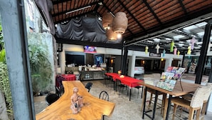 An outdoor dining area with wooden tables and chairs, a covered seating area, and a TV screen in the background. - Rcn Court (Chiang Mai)